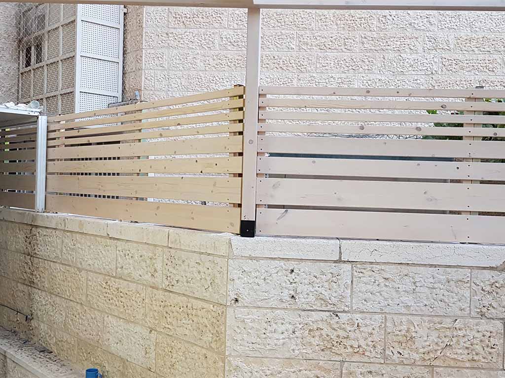 גדר מעץ בהיר מעל חומת אבן